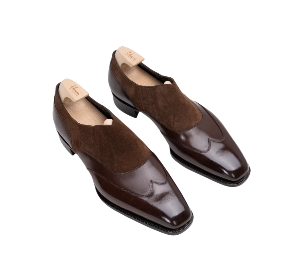 A pair of dark brown leather shoes with a suede panel and a pointed toe design.