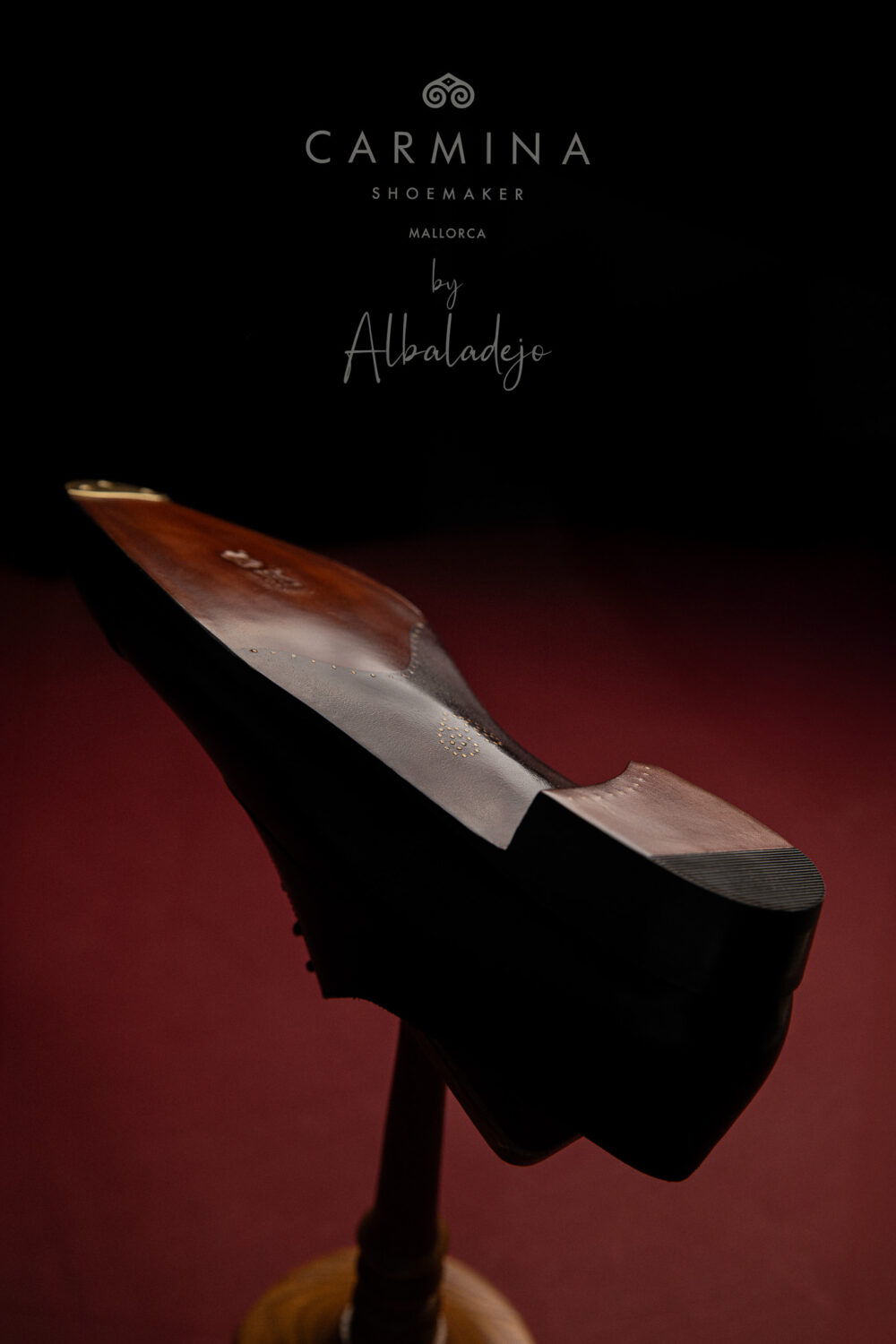 A wooden shoe last with a polished brown finish, displayed on a stand.