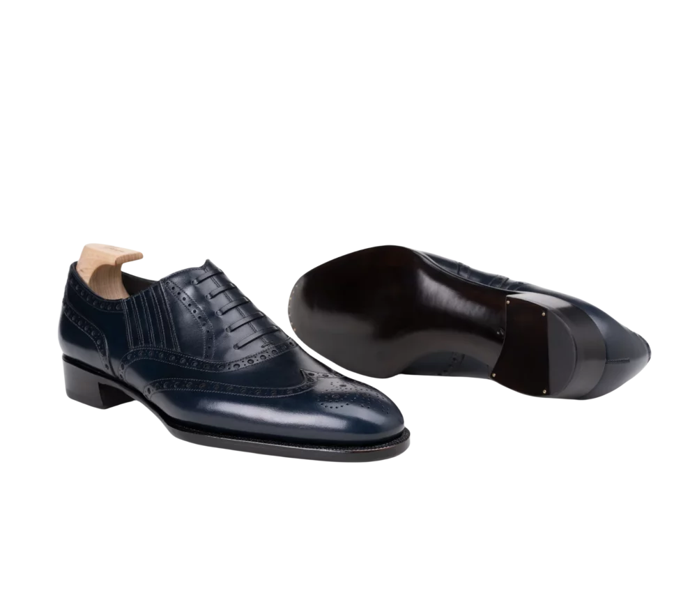A pair of navy blue leather dress shoes with brogue detailing and a wooden heel.