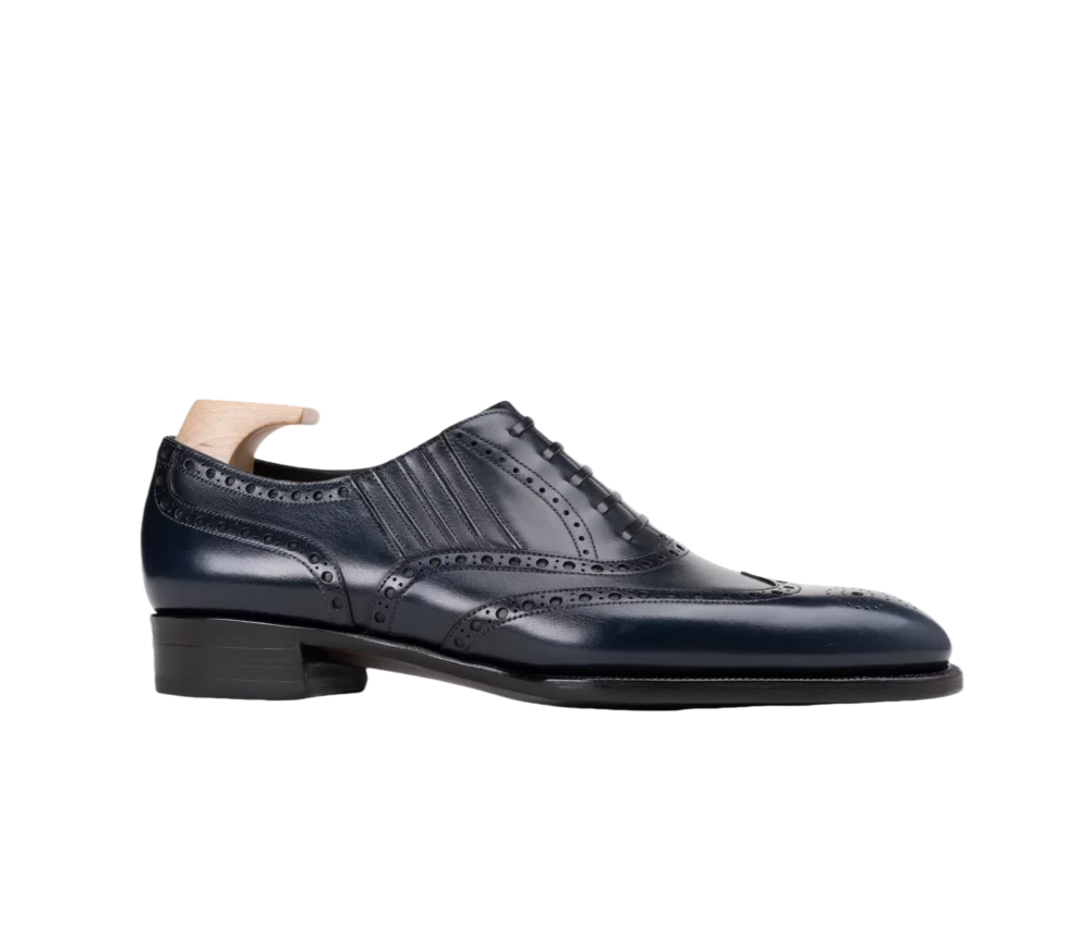 A dark navy leather dress shoe with brogue detailing and a wooden shoe tree.