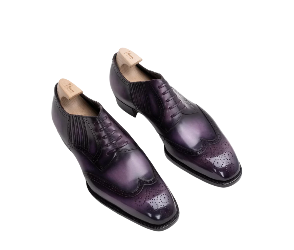 A pair of polished leather dress shoes in shades of purple with decorative perforations and a brogue design.