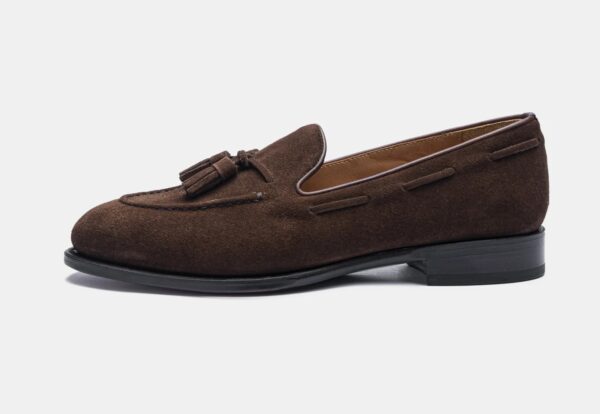 A brown suede loafer with a tassel detail and a low black heel.