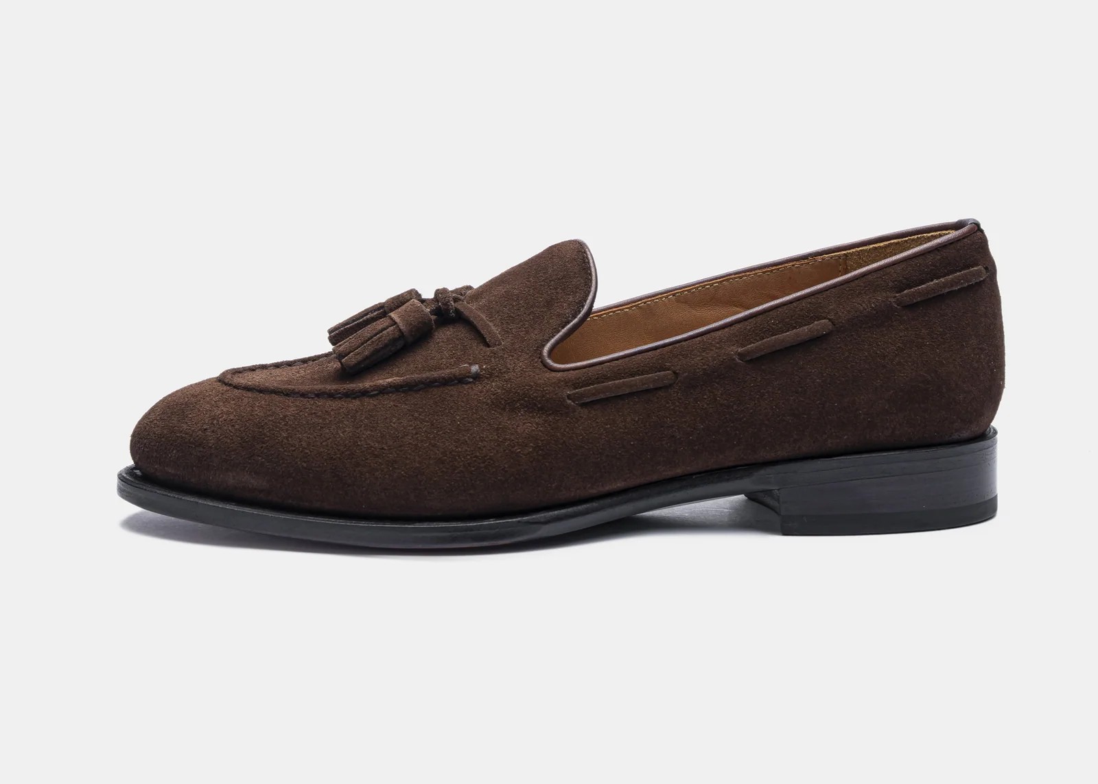 A brown suede loafer with a tassel detail and a low black heel.