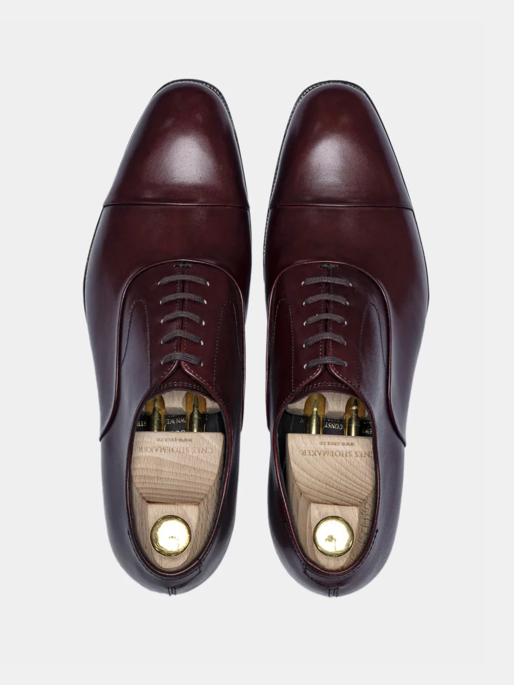 A pair of polished burgundy leather dress shoes with laces and shoe trees inside.