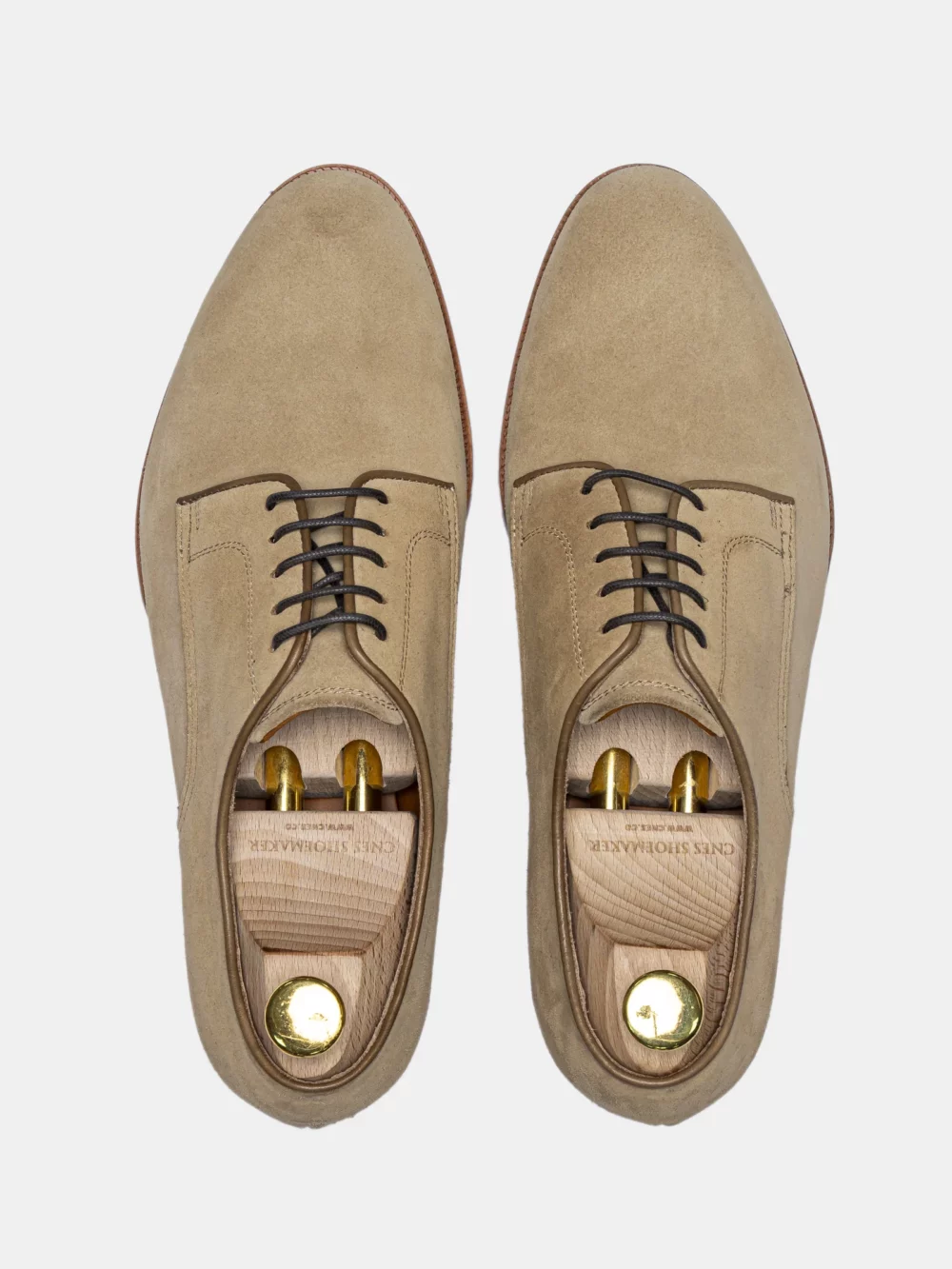 A pair of beige suede shoes with dark laces and wooden shoe trees inside.