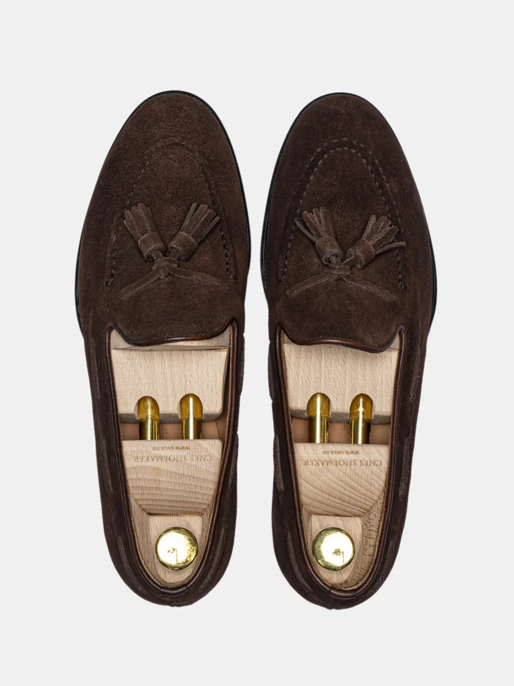 A pair of brown suede loafers with tassels and wooden shoe trees inside.