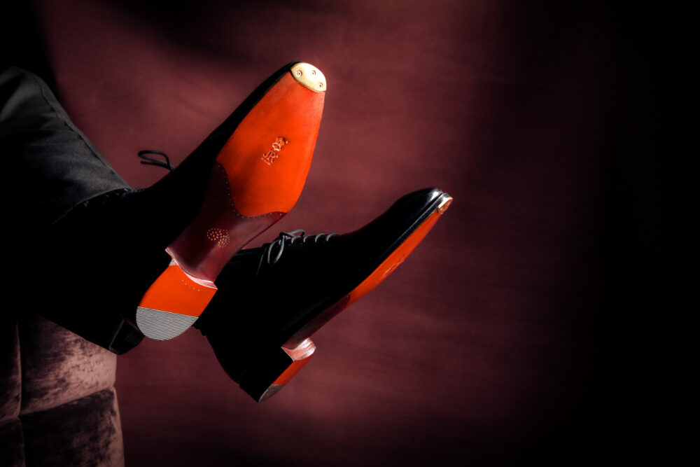 A pair of elegant black dress shoes with shiny red soles, positioned at an angle.