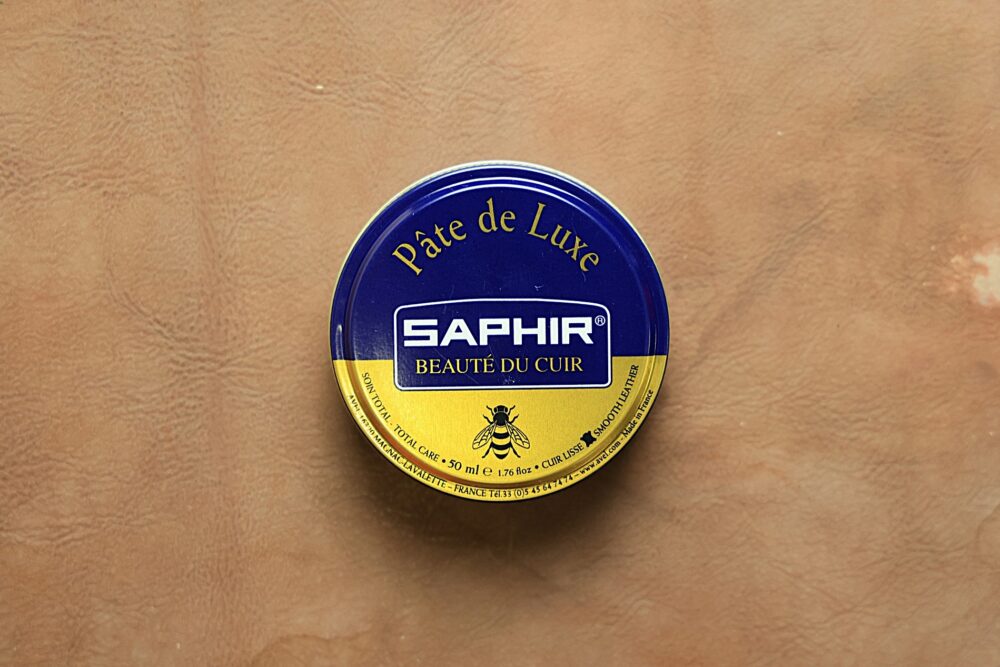 A round tin of Saphir Pâte de Luxe shoe polish, featuring a blue and yellow label.