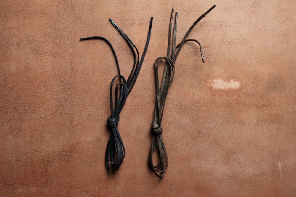 Two pairs of shoelaces, one black and one brown, are tied together on a textured brown surface.