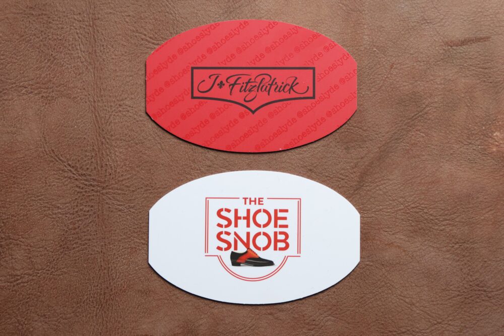 Two oval-shaped cards are displayed: the top card is red with the name "J. Fitzpatrick" in black, and the bottom card is white with "THE SHOE SNOB" in red and a shoe graphic.
