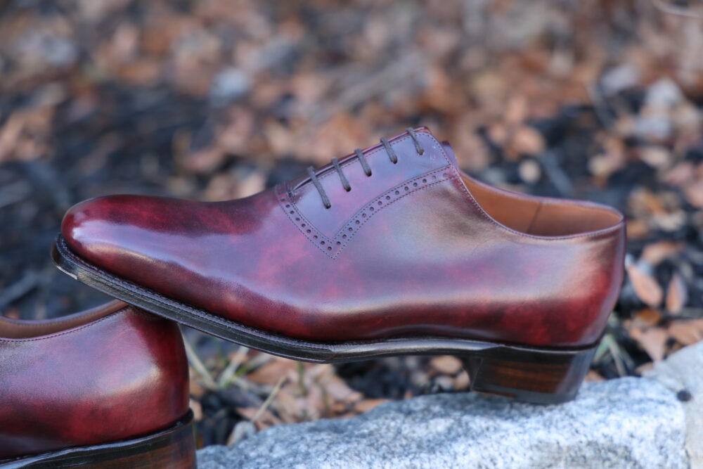 A polished burgundy leather dress shoe with a lace-up design and decorative perforations.