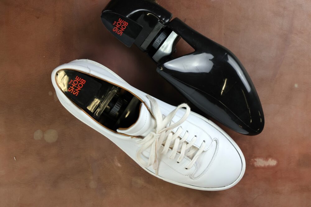 A white leather shoe with laces beside a black shoe tree.