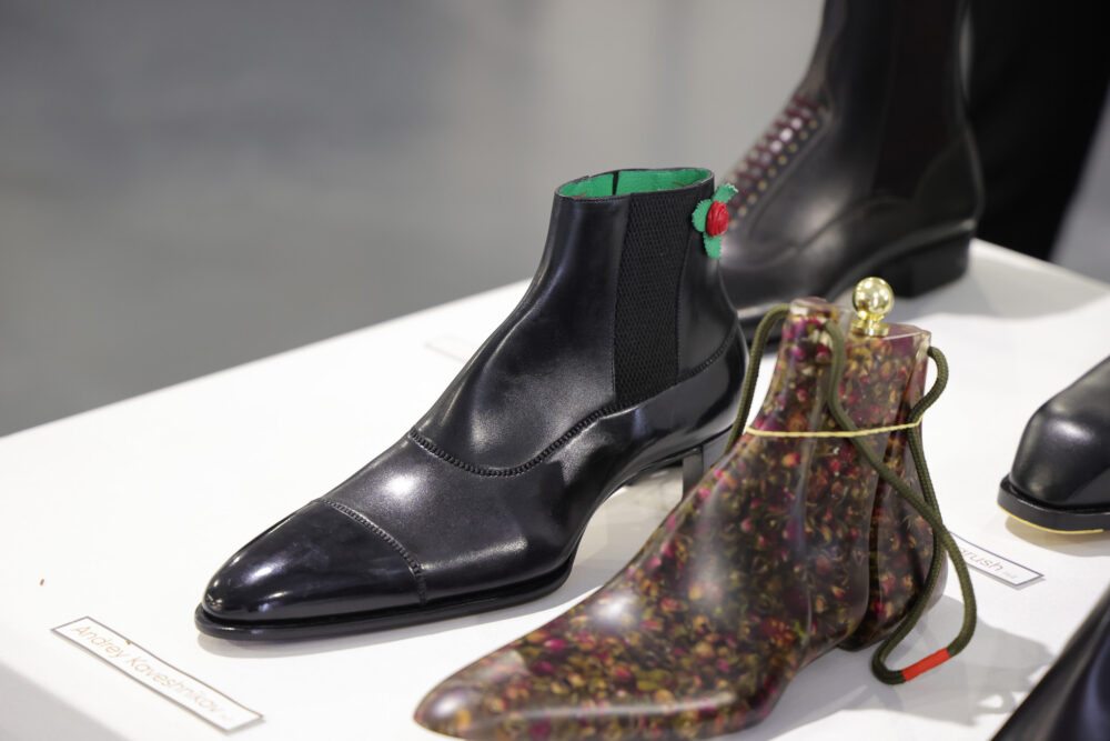 A pair of stylish black ankle boots with a green interior and a decorative red flower, alongside a translucent floral-patterned boot.