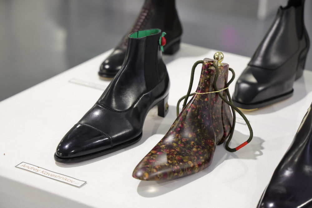 A pair of black leather ankle boots alongside a clear boot with a floral pattern and a green interior.