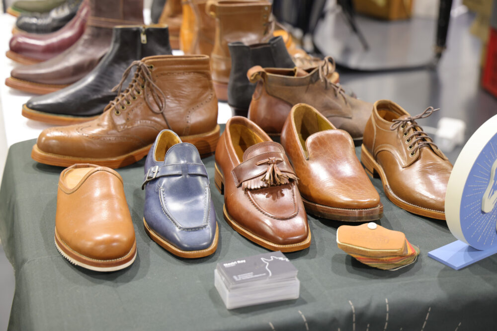 A variety of brown leather shoes, including boots, loafers, and dress shoes, displayed on a green table.