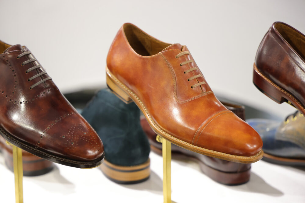 A polished tan leather dress shoe with laces and a rounded toe is displayed prominently.