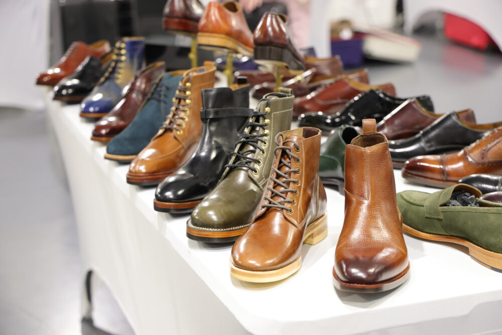A variety of leather shoes and boots in different styles and colors, including brown, green, and black, arranged on a table.