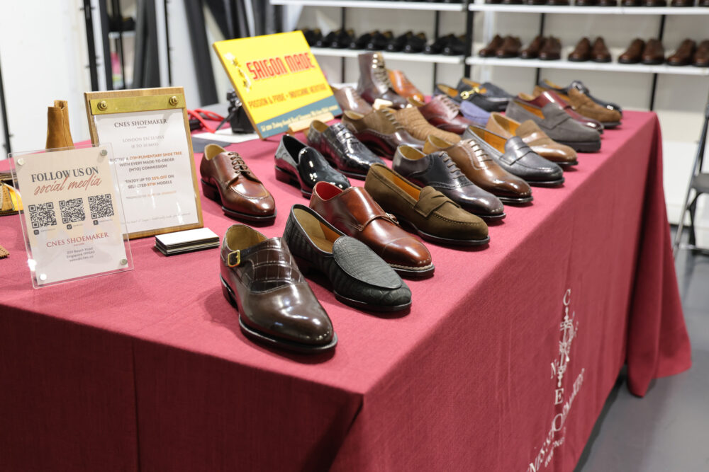 A display of various styles of brown leather shoes on a red tablecloth, with promotional materials nearby.