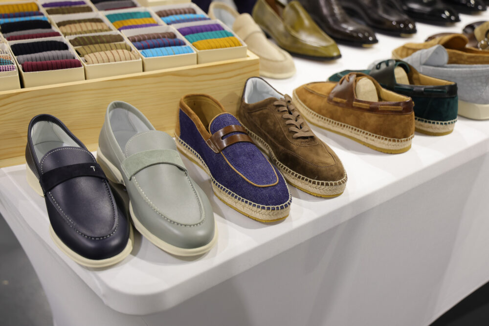 A collection of men's shoes in various styles, including leather loafers, suede sneakers, and casual slip-ons, in colors like navy, gray, brown, and green.