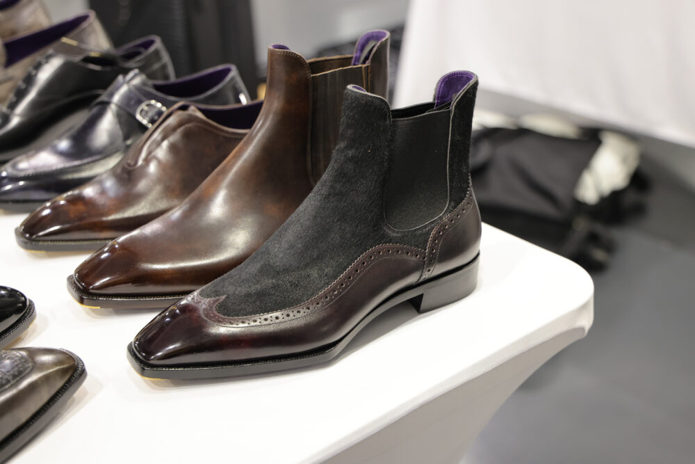 A polished dark brown and black leather ankle boot with a pointed toe and decorative brogue detailing.