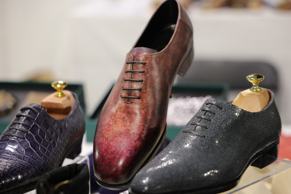 Three pairs of men's dress shoes in various colors and textures, including a burgundy leather shoe, a dark gray textured shoe, and a purple crocodile-patterned shoe.