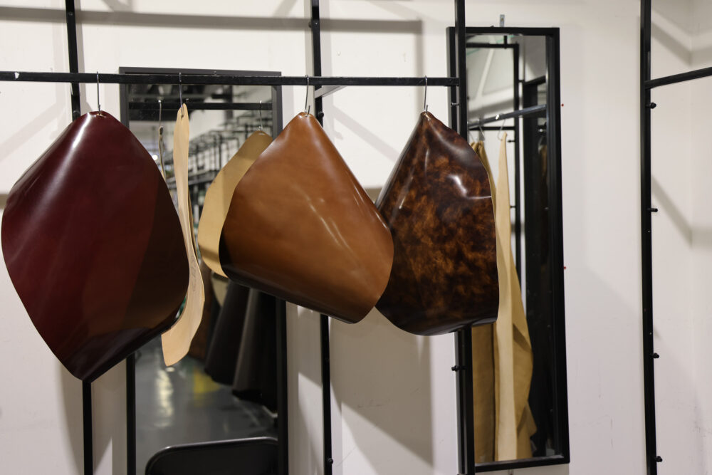 Various pieces of leather in shades of burgundy, brown, and tan are hanging on a rack.