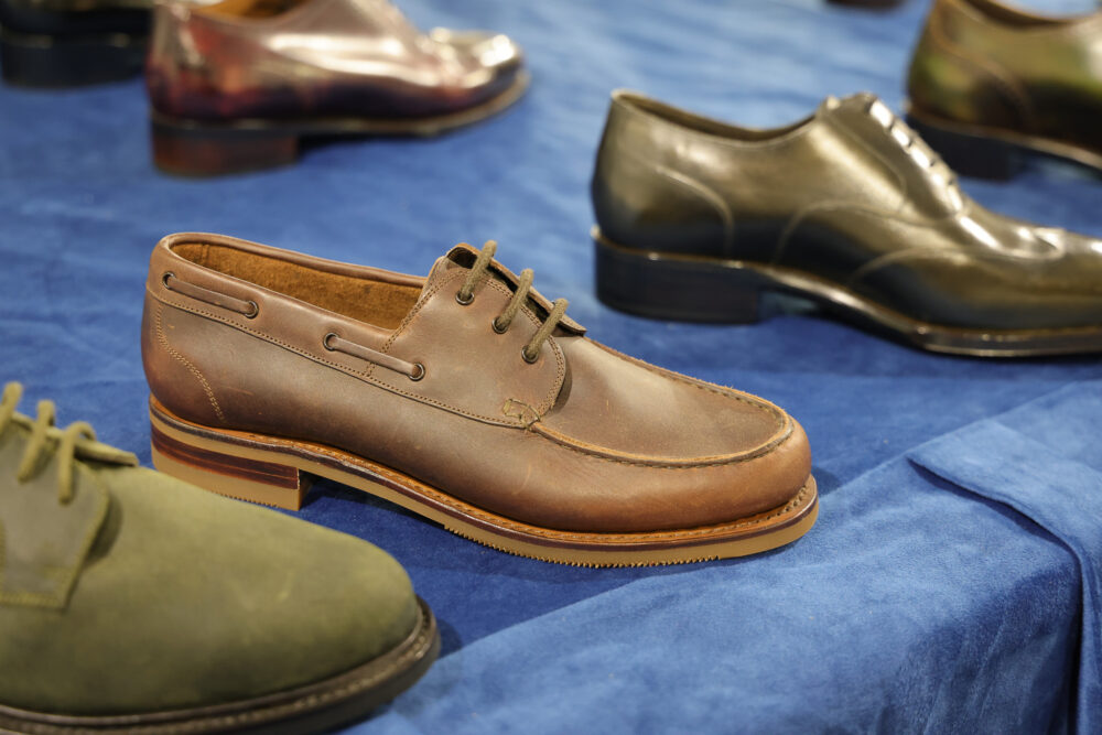 A brown leather shoe with laces and a contrasting sole is prominently displayed among other shoes.