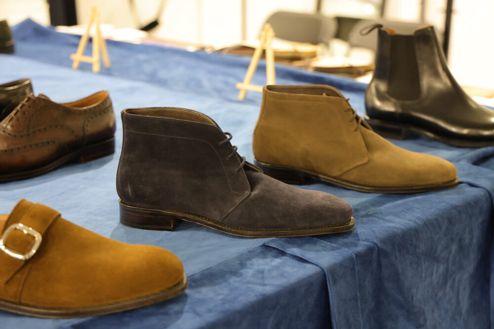 A selection of four pairs of shoes in various styles and colors, including brown leather, dark gray suede, light brown suede, and black leather.