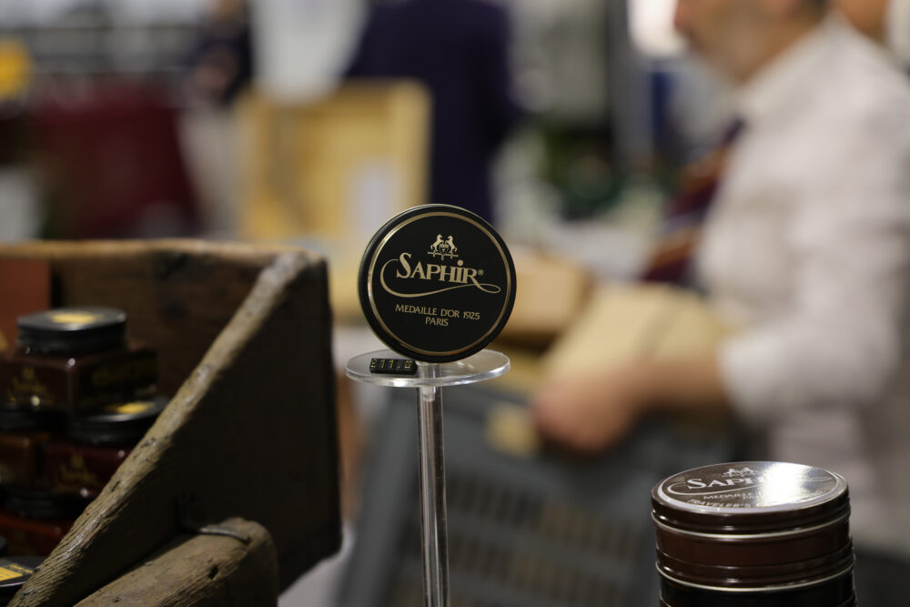 A black and gold Saphir shoe polish tin labeled "Médaille d'Or 1925 Paris" displayed on a clear stand.