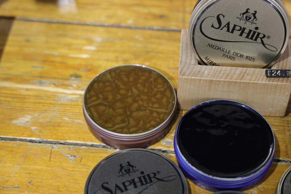 Three metal tins of shoe polish in shades of brown, black, and purple, labeled "Saphir."