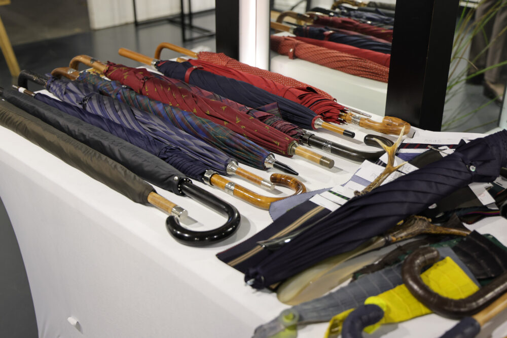A collection of various umbrellas with wooden and black handles, featuring colors like navy, burgundy, and patterned fabrics.