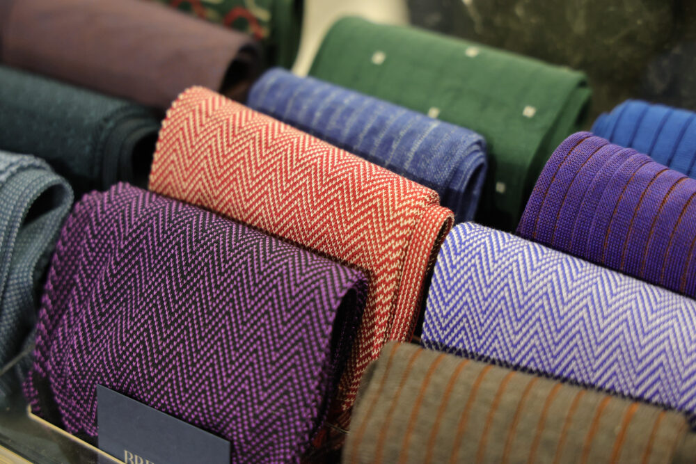 A variety of rolled fabrics in herringbone patterns, featuring colors like purple, red, blue, and green.