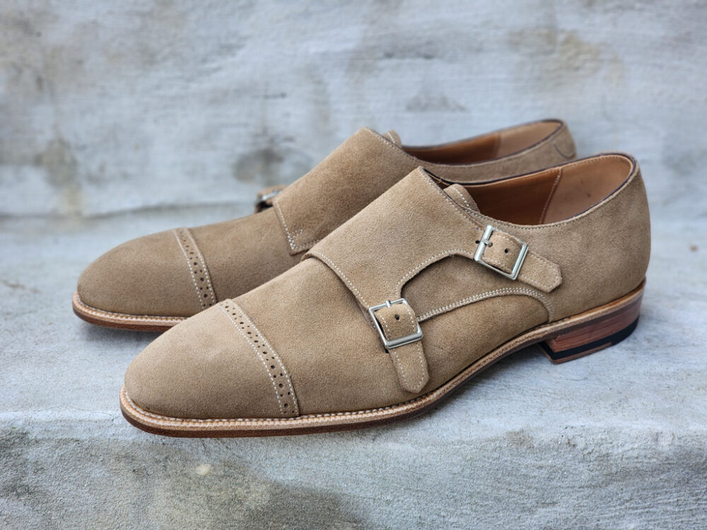 A pair of tan suede shoes featuring two silver buckles and a slightly pointed toe.