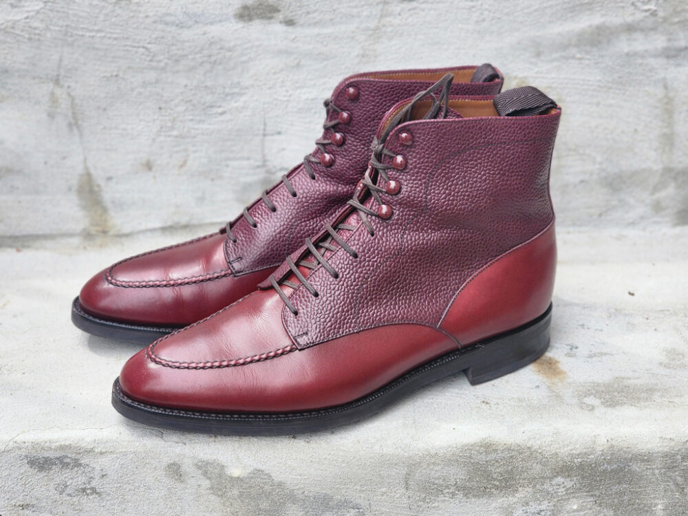 A pair of burgundy leather ankle boots with textured and smooth sections.