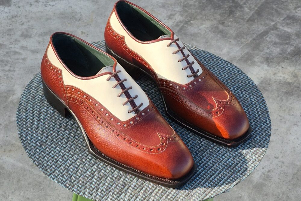 A pair of brown and cream leather dress shoes with decorative perforations and laces.