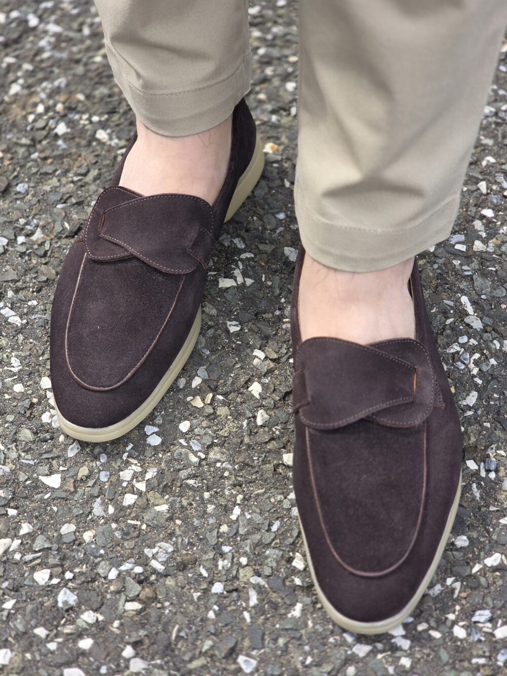 A pair of dark brown suede loafers with a light-colored sole, worn with khaki pants.