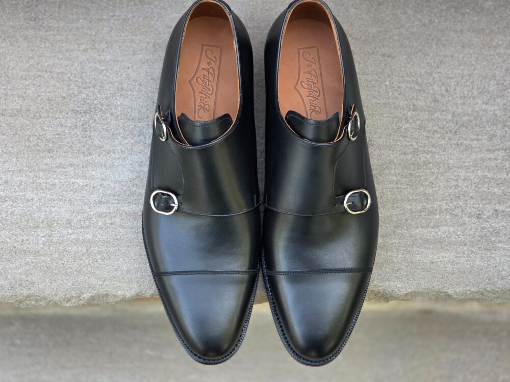Two black leather dress shoes with silver buckles on the sides.
