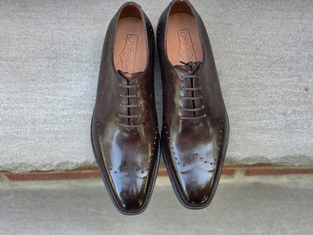 A pair of polished brown leather dress shoes with a pointed toe and decorative perforations.