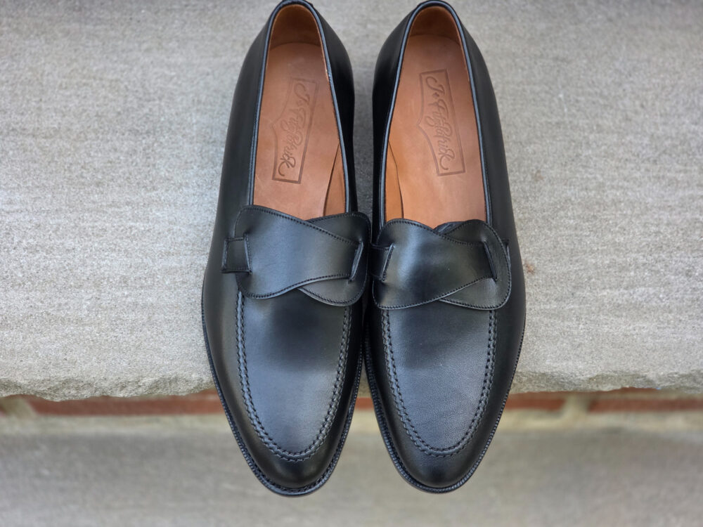A pair of black leather loafers with a decorative bow detail on the front.