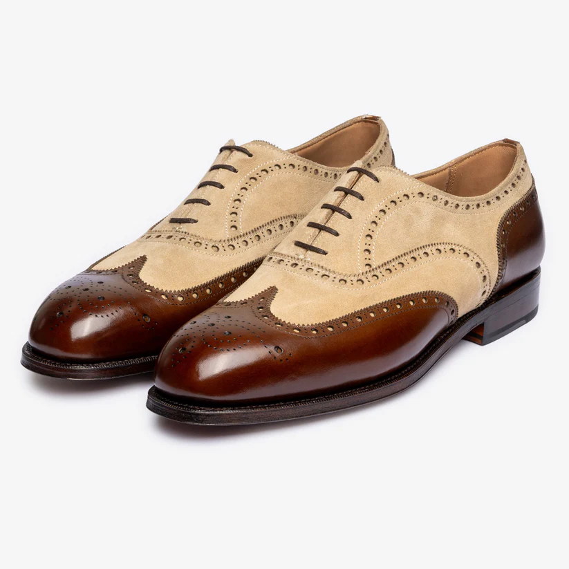 A pair of brogue shoes featuring a tan suede upper and a dark brown polished leather toe and heel.