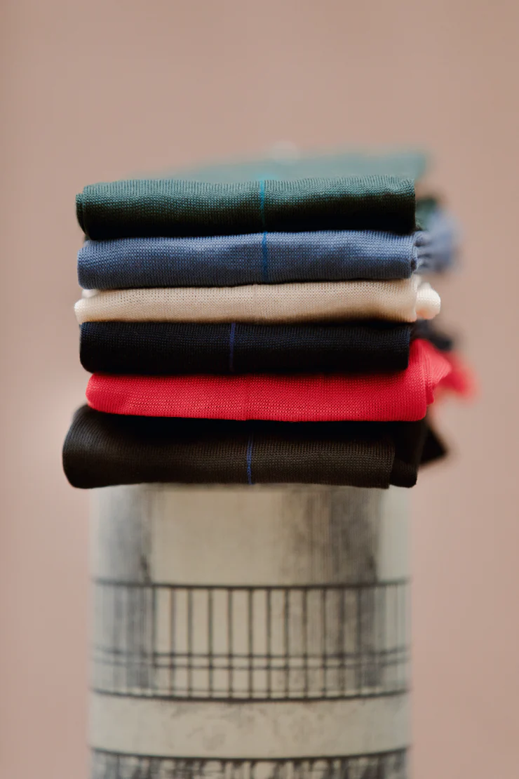 A stack of folded shirts in dark green, blue, cream, black, red, and dark brown on a cylindrical base.