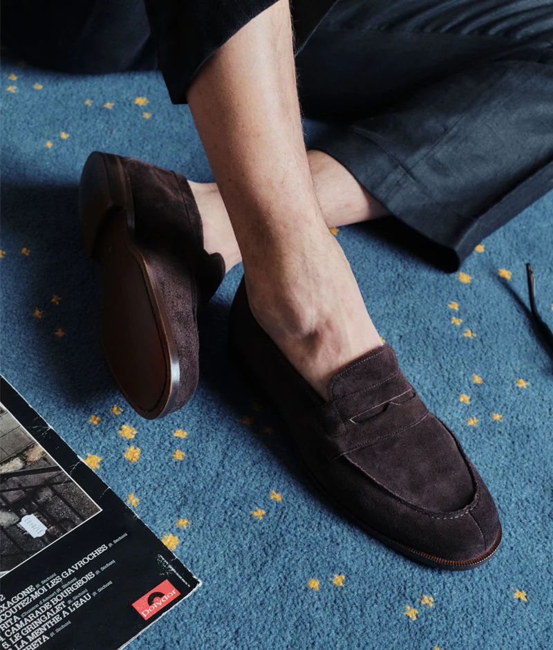 A close-up of a person's foot wearing dark brown suede loafers.