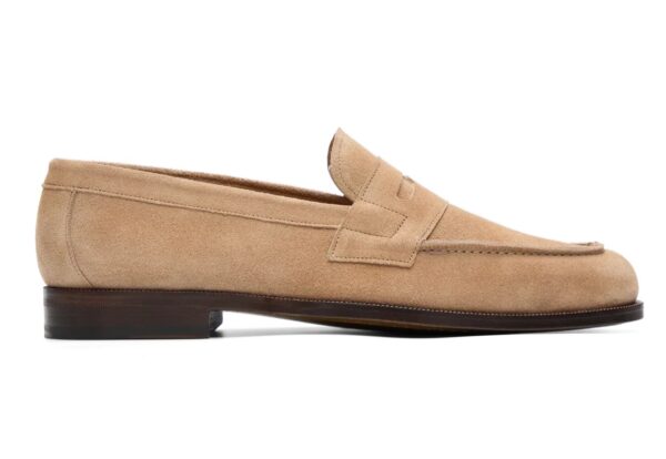 A tan suede loafer with a low heel and a decorative strap across the top.