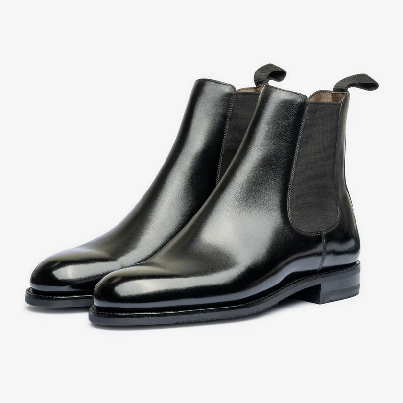 A pair of shiny black leather Chelsea boots with elastic side panels.