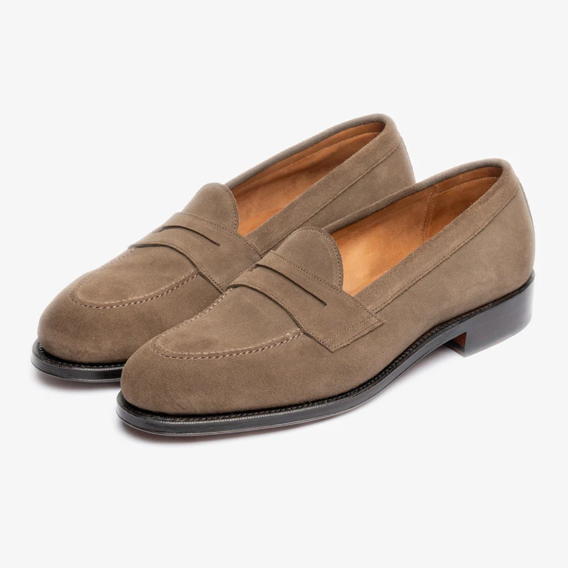 Brown suede loafers with a decorative strap detail and a low black heel.