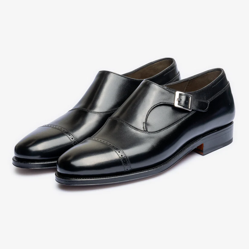 A pair of polished black leather dress shoes with a buckle detail and a cap-toe design.