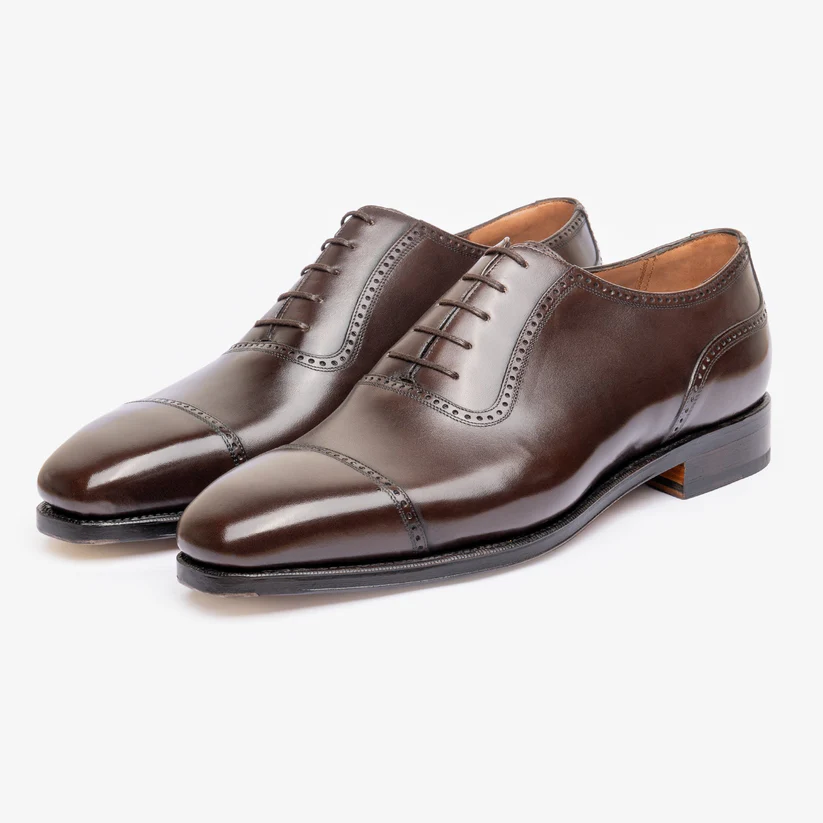 A pair of polished brown leather dress shoes with a cap toe and decorative stitching.