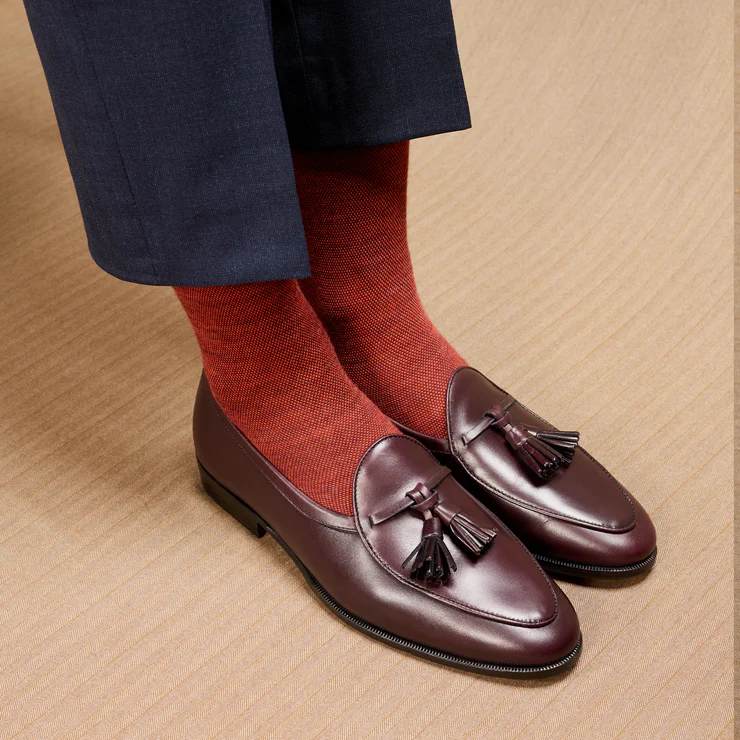 A pair of burgundy leather loafers with tassels, worn with textured red socks.