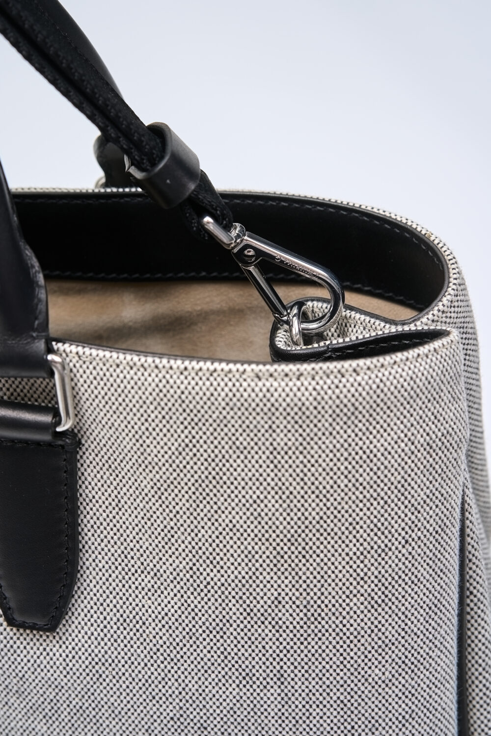 A close-up of a textured gray handbag with a black leather strap and silver hardware.