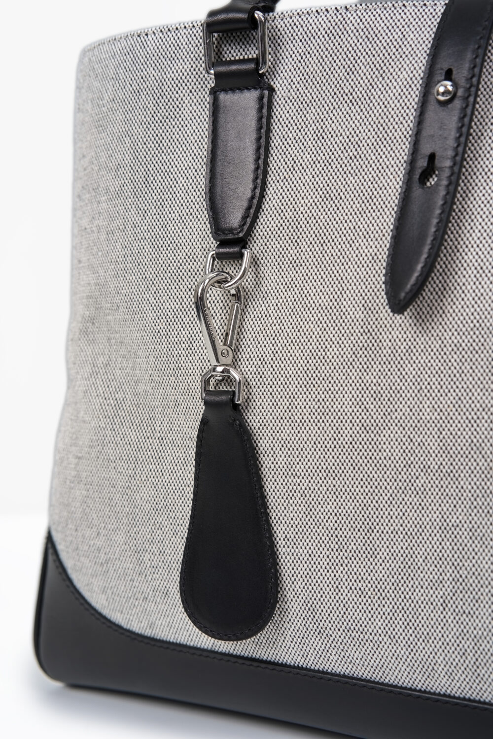 A close-up of a textured gray handbag featuring a black leather strap and silver hardware.